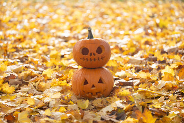 Two carved pumpkins stacked on a bed of vibrant autumn leaves, showcasing Halloween spirit and...