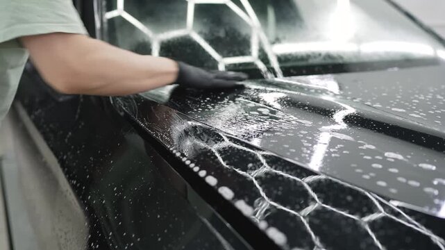 Professional car detailer applying protective film on black car hood