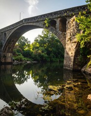 Ancient stone arch bridge over a calm river, reflecting a perfect circle