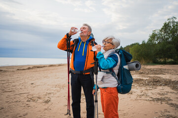 Hiking tourism adventure. Senior couple man woman drinking water enjoying outdoor recreation hiking on beach. Old people backpackers hikers enjoy walking hike trekking active vacation beauty of nature
