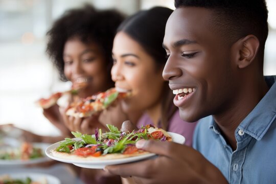 African American man and diverse friends smile, happily eating delicious pizza meal together.