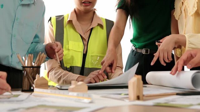 Smart architect and safety engineer discussion about building blueprint on table with architectural document, measurement tools and wooden block scatter around at modern office. Closeup. Delineation.