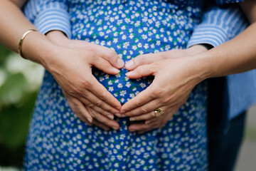 Pregnant couple holding hands on belly in heart shape, celebrating new life