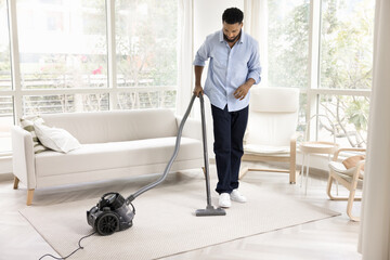 Young male vacuuming carpet on floor with washing vacuum cleaner