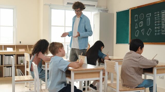 Skilled teacher walking at classroom while looking at student homework. Professional instructor checking smart children notebook while student doing test or working on homework at classroom. Pedagogy.