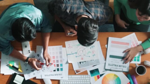 Top down aerial view of project manager looking at screen while designer writing idea. Smart business team explain idea of logo design while designer choose theme while looking at palette. Symposium.