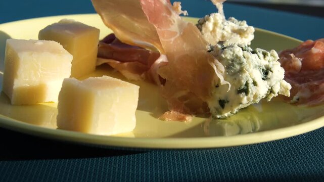 Cheese prosciutto fork Charcuterie board, cheese platter, a hand pricks a cube of gouda cheese with a wooden toothpick