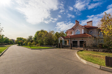 Beautiful suburban street with a spacious home surrounded by greenery on a sunny day. The clear blue sky and warm sunlight create a serene atmosphere