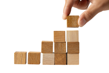 A hand places a light-brown wooden cube atop a growing staircase of similar cubes