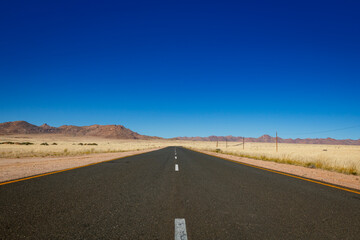 Endless road in the middle of savanna lading to mountains