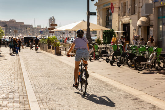 Jeune femme &agrave; v&eacute;lo sur la piste cyclable de la Canebi&egrave;re en direction du Vieux-Port de la ville de Marseille, vue de dos portant un casque, un T-shirt et un short en jean