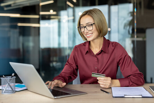 Happy businesswoman making online payment using credit card and laptop in office