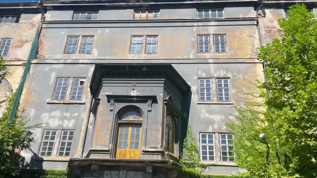The image shows an abandoned multistory building with a faded faade and overgrown vegetation