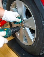 Close-up of hands in white gloves using a drill to remove a wheel lug nut