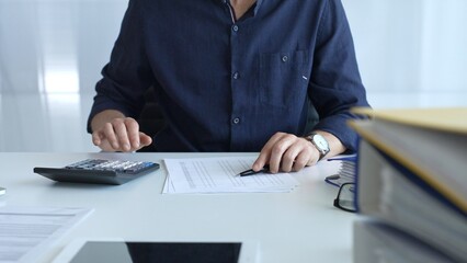 Professional businessman calculating financial data, reviewing documents near laptop in modern workplace setting. Audit and taxes, business concept