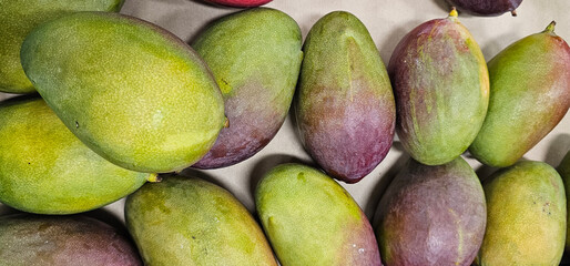 A close-up view of ripe mangoes with a mix of green and purple skin. The fruit looks fresh and ready for consumption, showing vibrant natural colors.