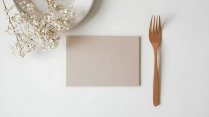 Minimal table setting with blank card mockup, golden fork, ceramic plate, and dried flowers on white background, elegant design template for restaurant, menu, or event branding.