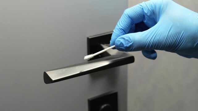 A forensic scientist wearing protective gloves and using a cotton swab takes a sample from a doorknob and searches for evidence.
Crime scene work.
Laboratory examination of fingerprints.