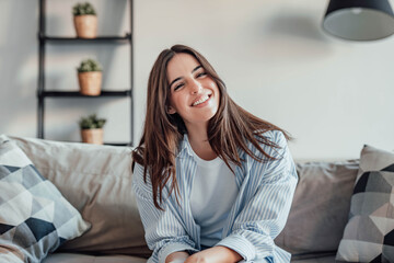 Naklejka premium Young attractive cheerful lady sitting on sofa, relaxing looking at the camera at home. Beautiful brunette woman on her 30s chatting on video call online