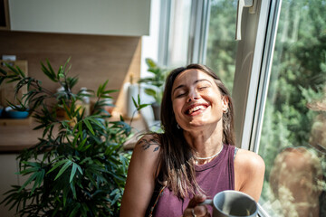 Happy woman drinking coffee by the window in a sunny kitchen