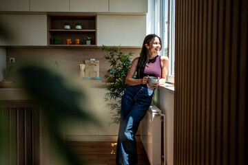 Young woman enjoying a cup of coffee by the window in a modern kitchen