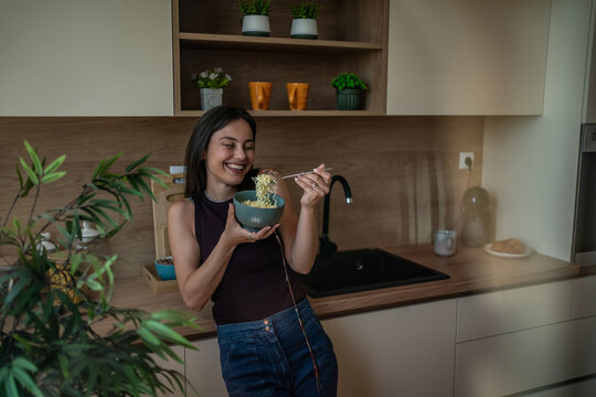 Young woman enjoying noodles in modern kitchen