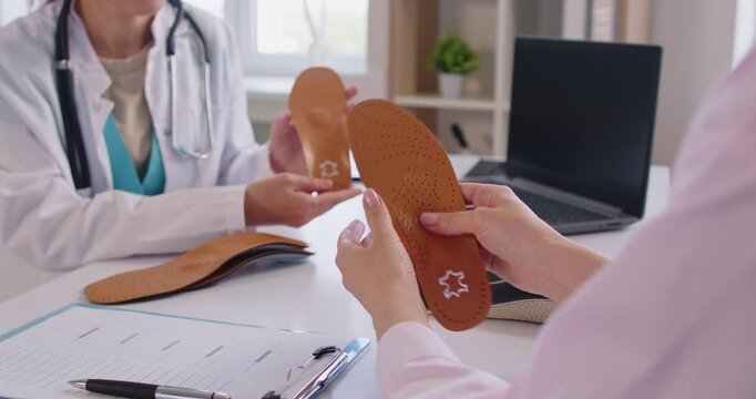 Medical office of orthopedist doctor, discussing orthotic insoles with patient holding and examining, medical consultation for foot care, professional guidance to help comfort from heel to toe