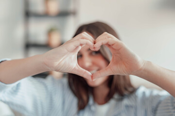 Beautiful woman showing heart sign with folded fingers smiling looking at camera, head shot...