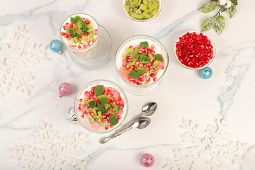 Kiwi and pomegranate parfait on a bright festive table, an idea for decorating food and decorating New Year's dishes. Banner for the screen, template for creativity. Christmas and New Year's dishes.