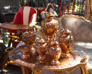 A table with a tray of copper vases and a chair. The vases are arranged in a row and the chair is placed behind them. City of Puebla, Mexico, crafts