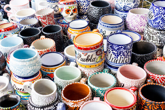 A collection of colorful ceramic cups with various designs and patterns, including one that says "PuBla" and "India". City of Puebla, Mexico, crafts
