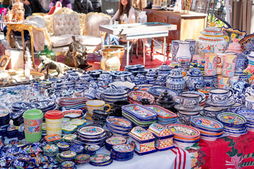 A table full of blue and white dishes. The table is set up in a market. There are many different types of dishes on the table. City of Puebla, Mexico, crafts