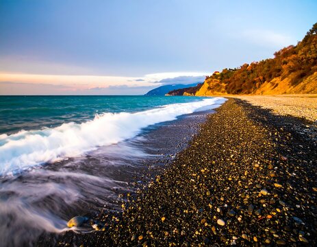 Coastal sunset scene. Foamy waves on a dark pebble beach