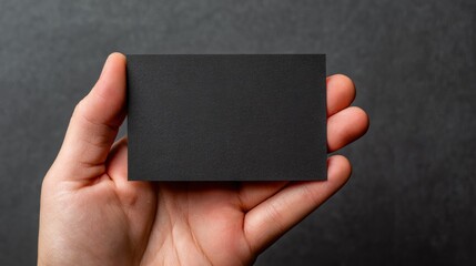 Unique black business card held in a hand against a dark textured background for branding ideas