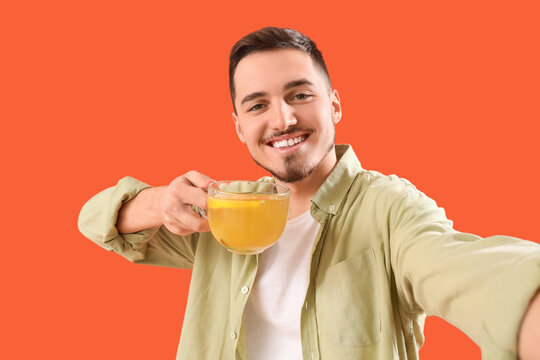 Young man with cup of lemon tea taking selfie on orange background, closeup - Powered by Adobe