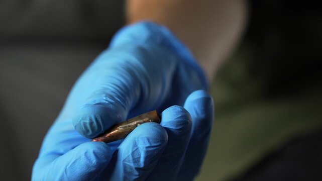 A forensic scientist wearing latex gloves holds a bullet in his hand at a crime scene.
Murder scene and police officer holding evidence.
Forensic scientist work and murder investigation.
Crime scene