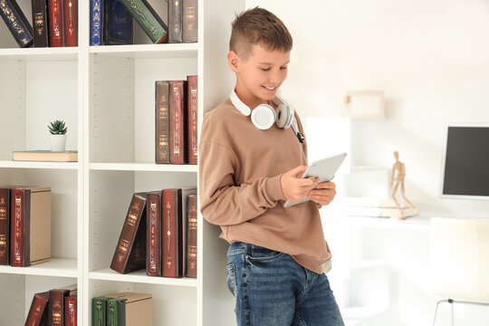 Teenage boy with tablet computer near bookshelf in library