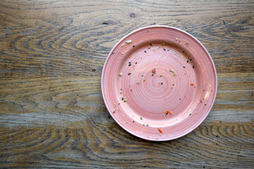 Top view of empty dirty pink ceramic plate with food leftovers and crumbs on rustic wooden table, concept of food waste, dining, restaurant cleanup, hygiene, and sustainable lifestyle.
