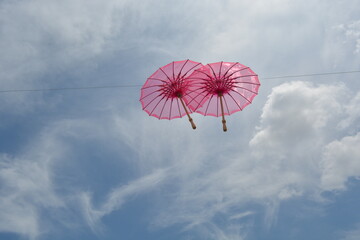 A line of vibrant pink umbrellas suspended against a bright blue sky with wispy clouds
