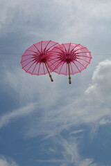 A line of vibrant pink umbrellas suspended against a bright blue sky with wispy clouds