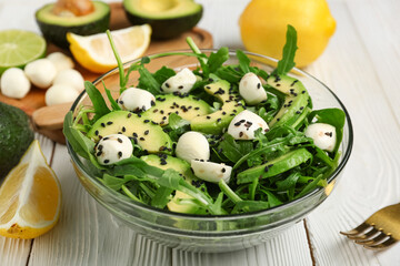 Bowl with healthy arugula salad on white wooden background, closeup