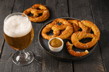 Composition with glass of cold beer and pretzels on black wooden background, closeup
