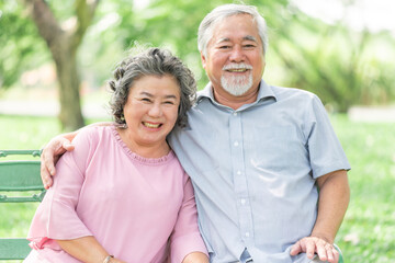 Happy smile mature senior Asain couple sitting on the bench in park enjoying retirement and spending time together. Elderly people love, care and relationship concept.