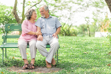 Happy smile mature senior Asain couple sitting on the bench in park enjoying retirement and spending time together. Elderly people love, care and relationship concept.