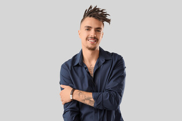 Tattooed young man with dreadlocks on light background