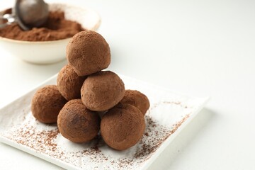 Tasty chocolate candies with cocoa powder on white table, closeup. Space for text