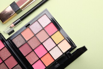 Eyeshadow palettes and other makeup cosmetics on light green background, flat lay. Space for text