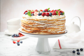 Delicious crepe cake with fresh berries on white marble table