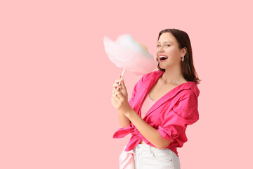 Beautiful young happy woman with cotton candy on pink background