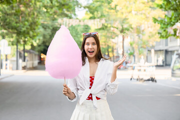 Beautiful young surprised woman with cotton candy in park, outdoors